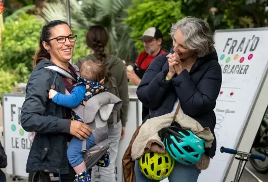 Une femme portant son bébé discute avec une autre femme, les deux sourient. 