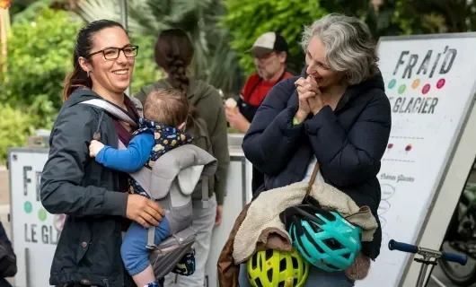 Une femme portant son bébé discute avec une autre femme, les deux sourient. 