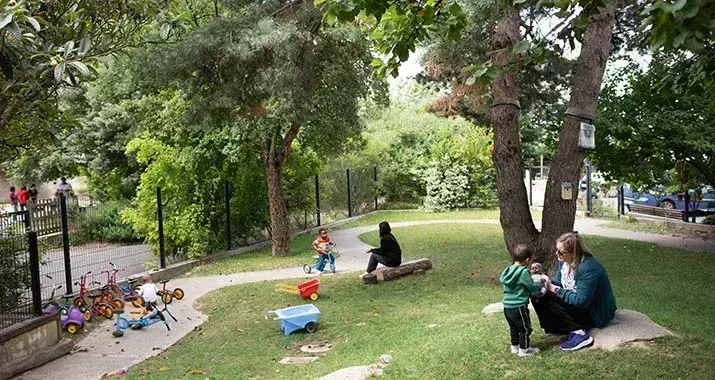 Dans le jardin de la crèche Manufacture, à Nantes, une éducatrice joue avec un enfant. L'environnement est très vert, avec pelouse et arbres. 