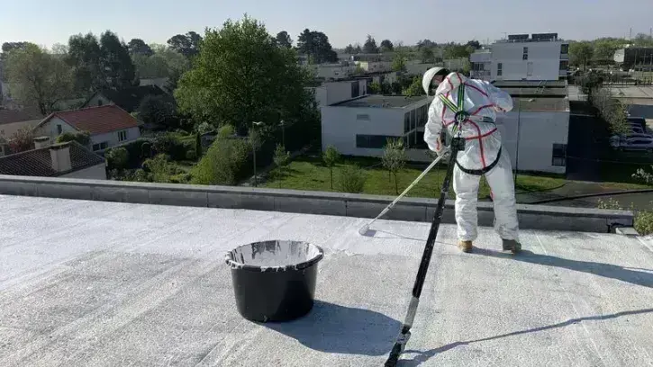 Un ouvrier applique une peinture blanche sur le toit d'un bâtiment.