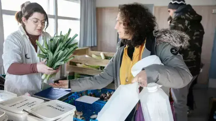 Une bénévole de l'épicerie VRAC sert des poireaux à une cliente adhérente à ce réseau d'achat groupé de quartier..