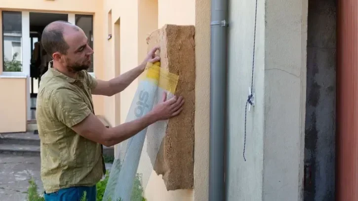 Un homme installe un panneau isolant sur la façade de sa maison.