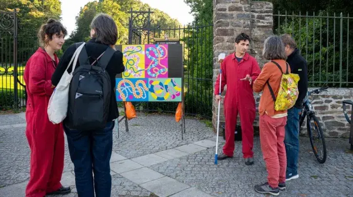 Deux artistes en bleu de travail collent des affiches et discutent avec des habitants à l'entrée du parc de la Gaudinière.