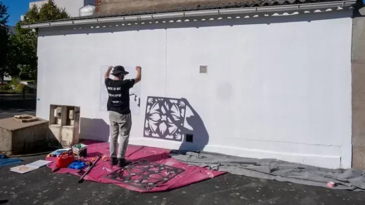 Une personne peint une fresque sur la façade de l'ancien café de la gare de Vertou.