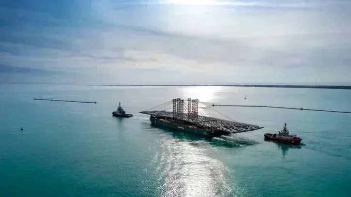 Vue de drone de la barge chargée du tablier, encadrée par deux remorqueurs.