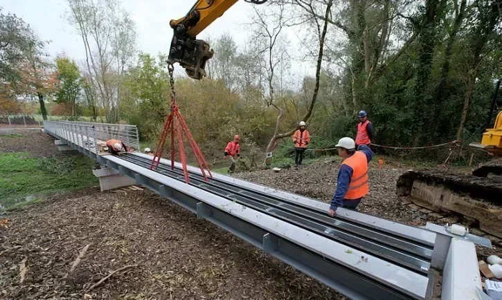 Une grue dépose le dernier tronçon d'une passerelle métallique. 