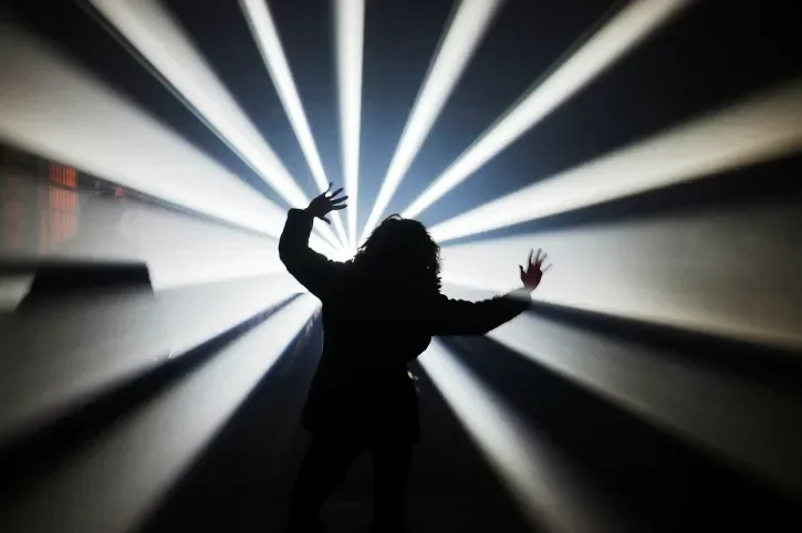 Un homme danse sous les projecteurs d'une salle de musique électronique.