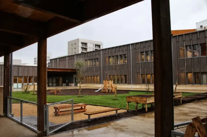 Point de vue depuis un préau de la cour végétalisée de l'école Joséphine Baker et du bâtiment à la façade en bois. 