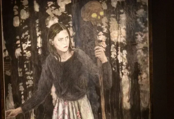 Une oeuvre d'Iris Von Dongen, intitulée Into the Wood, représente une femme aux long cheveux bruns, dans les bois portant un pic coiffé d'une tête de mort.  