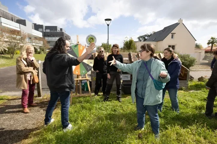 Deux personnes se tapent la main devant un compost collectif, tandis que d'autres les regardent et sourient.