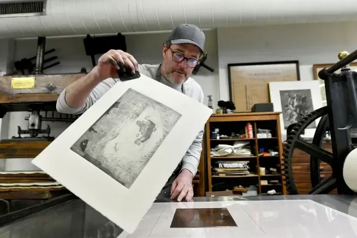 Un homme tient une gravure entre ses doigts. 