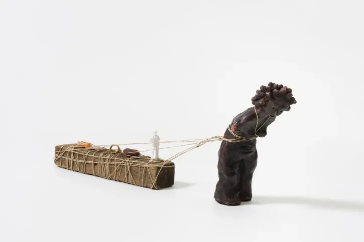 Une sculpture en bois représentant une femme lestée de petits personnages.