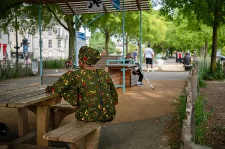 Une femme de dos sur un banc, à l'ombre des arbres de la place de la Petite-Hollande.