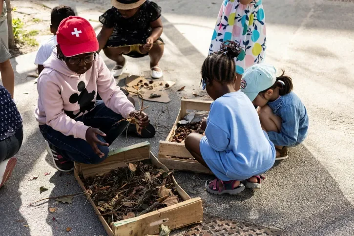 Des enfants devant des cagettes de branches et de feuilles mortes.