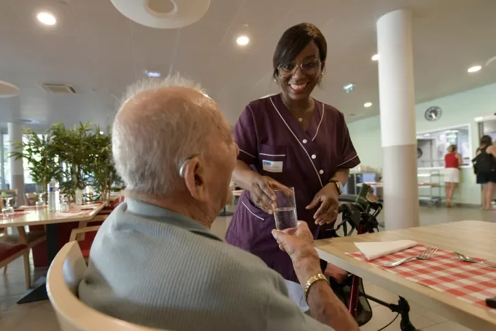 Une aide-soignante donne à boire à un senior.