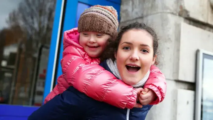 Une jeune femme poste une enfant trisomique sur ses épaules, les deux sourient