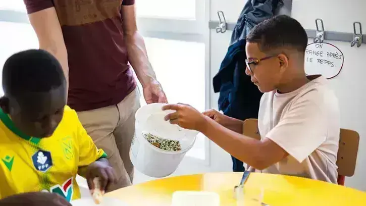 Youssef vide les restes de son assiette dans le seau qui permettra de mesurer le gaspillage du repas végétarien du jour de la cantine de l'école Joséphine Baker à Nantes © Garance Wester pour Nantes Métropole